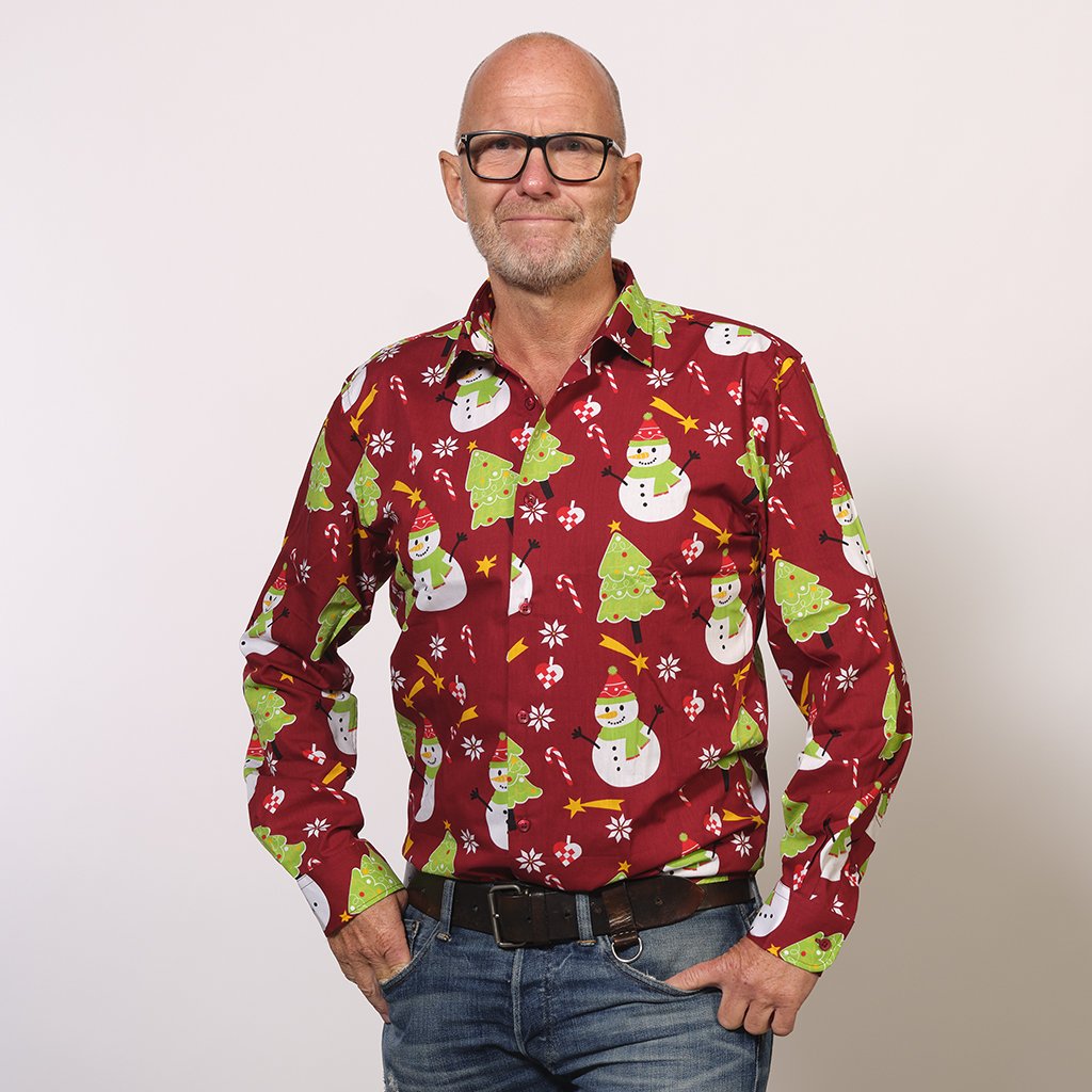 En man klädd i en röd jultröja med tomtar och julgranar på.