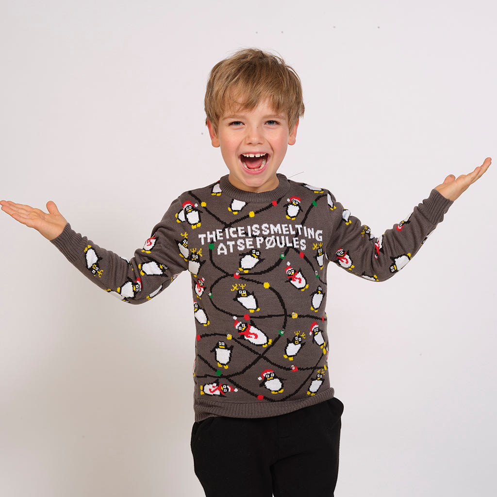 Ett barn i en grå jultröja med pingviner och ljus.