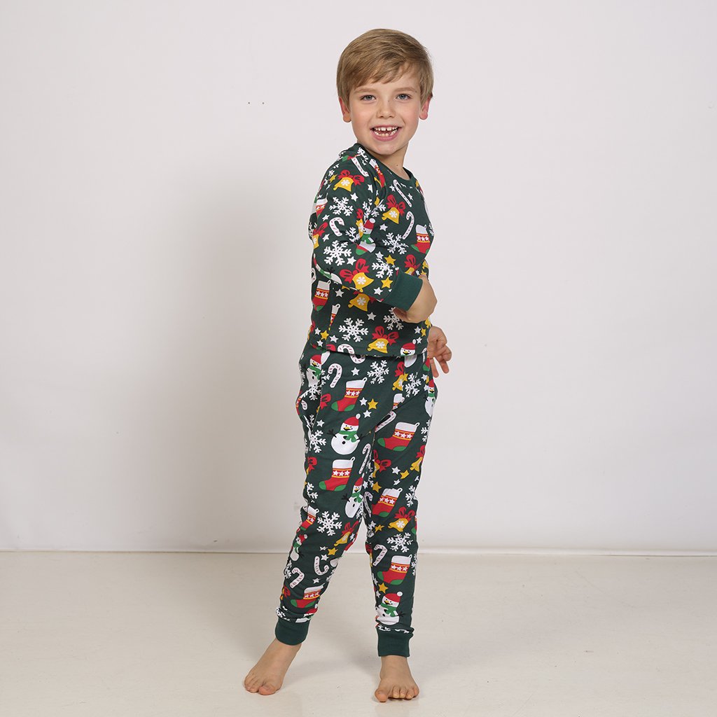 Barn i mörkgrön julpyjamas med snöflingor, snögubbar, polkagrisar och bjällror.