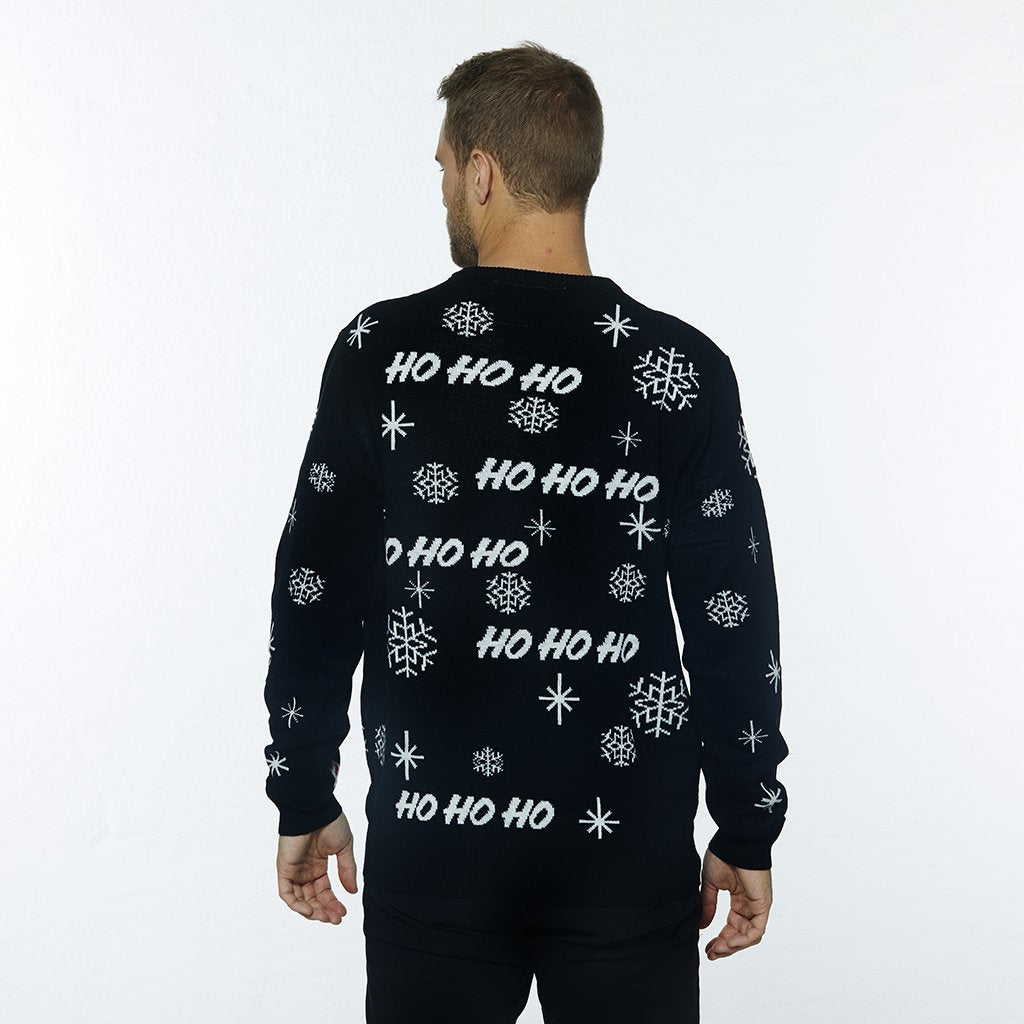 En man med ryggen vänd bär en svart jultröja med en jultomte och snöflinga på den.