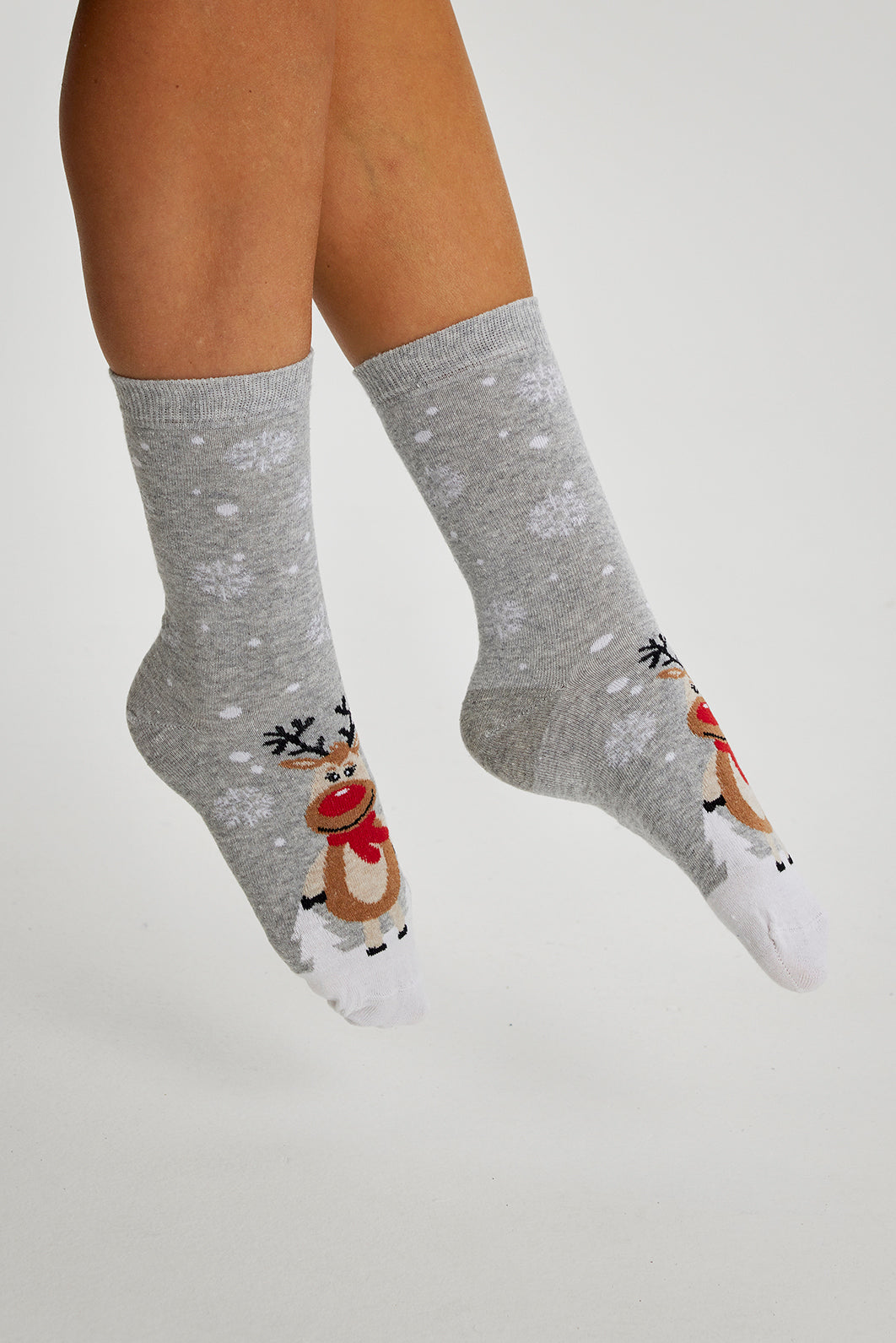Ett par fötter i grå julstrumpor med renar på.
