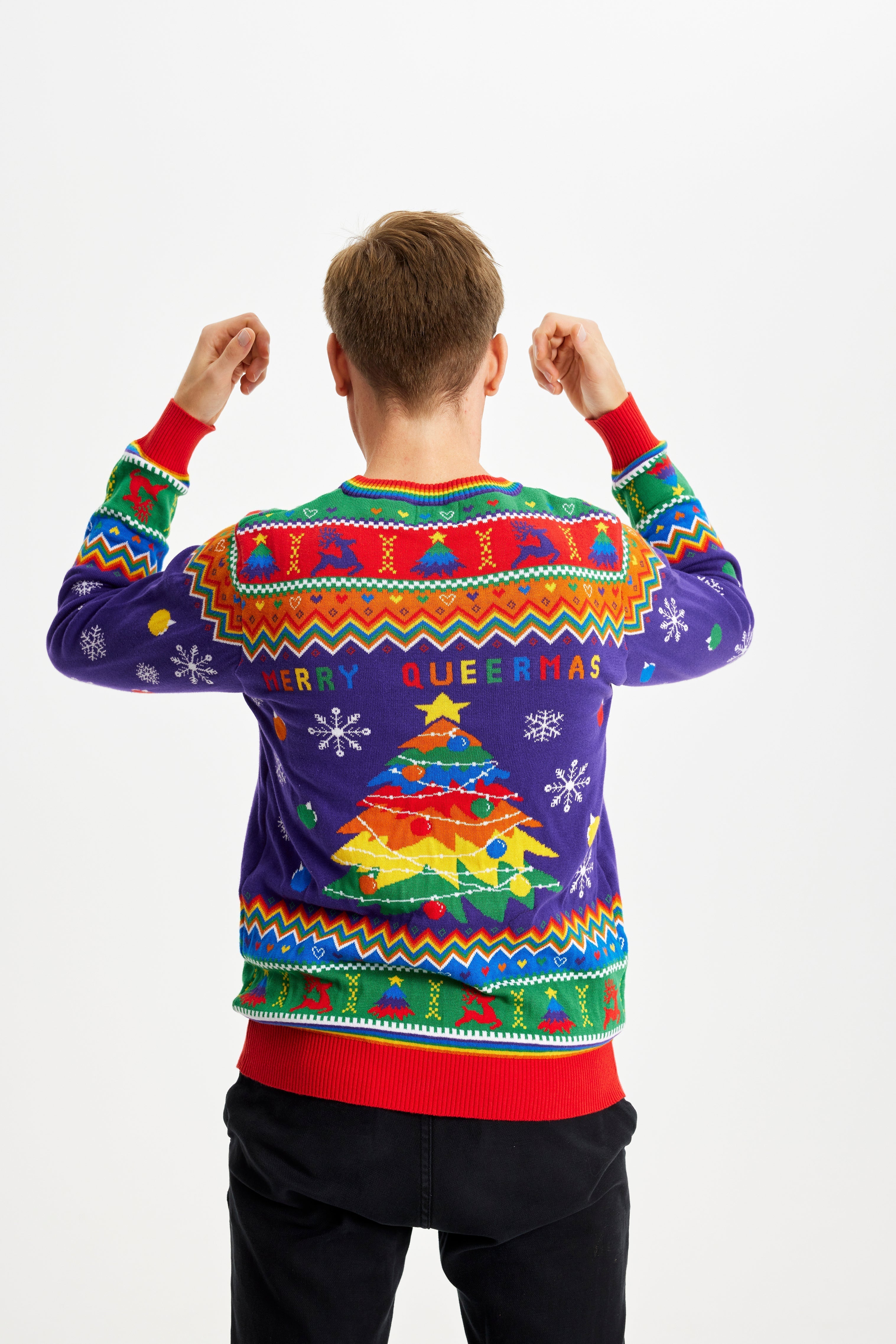 En man med ryggen vänd och händerna i luften klädd i en regnbågsfärgad jultröja med texten 