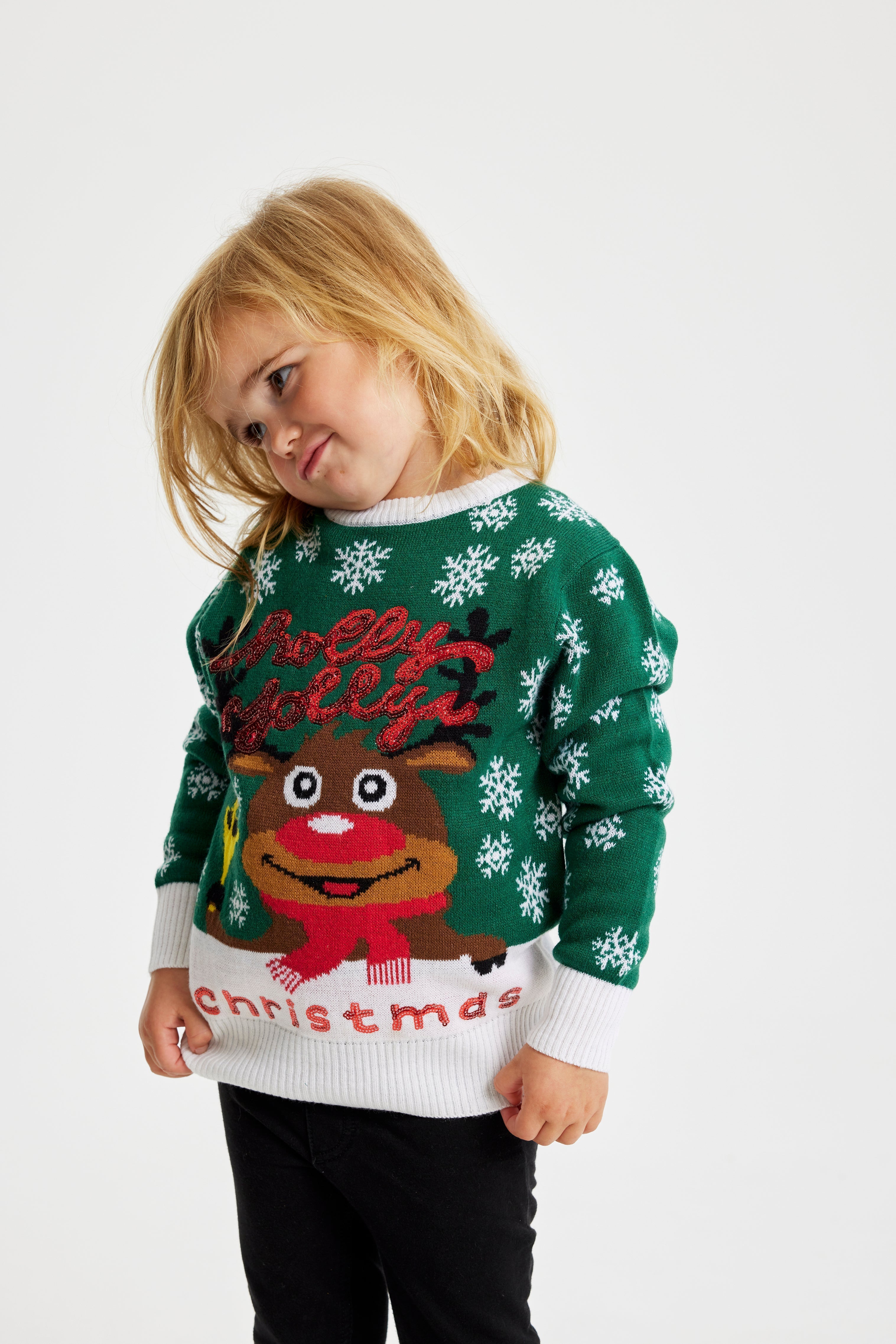 Ett barn i en grön jultröja med en ren och en snöflinga.
