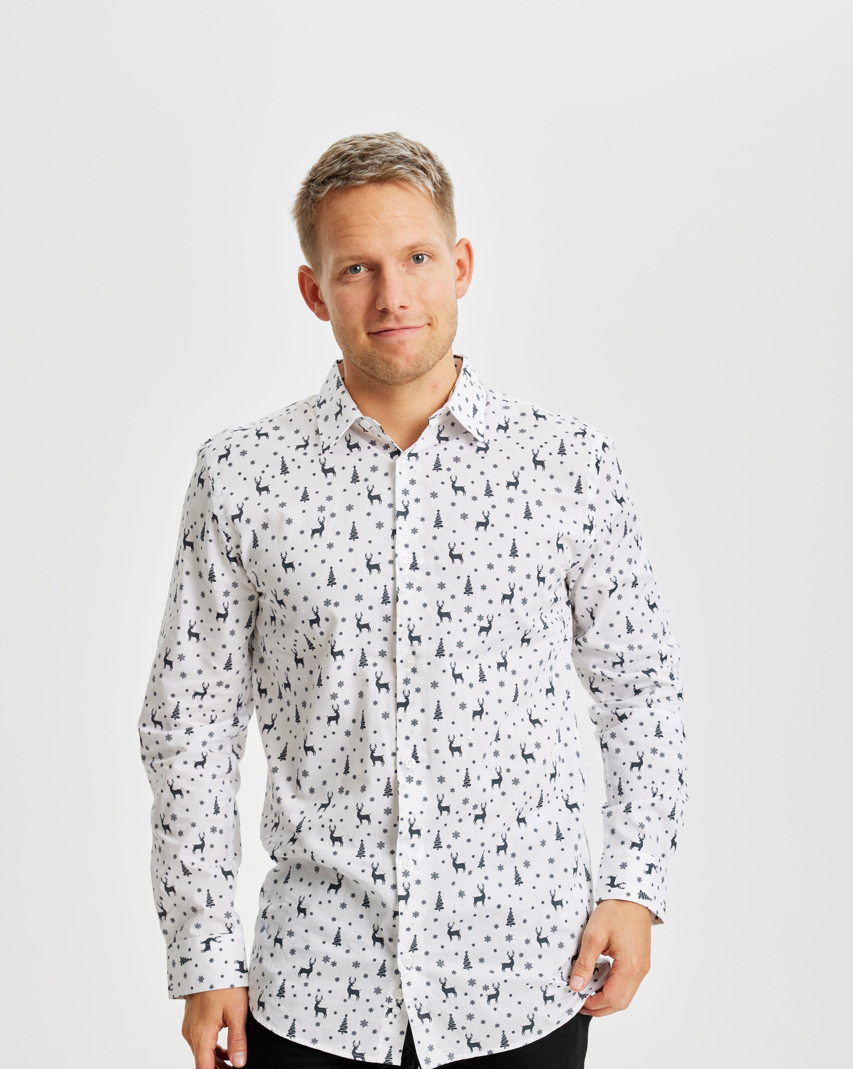 En man i sidled klädd i en vit jultröja med julgranar och renar på.
