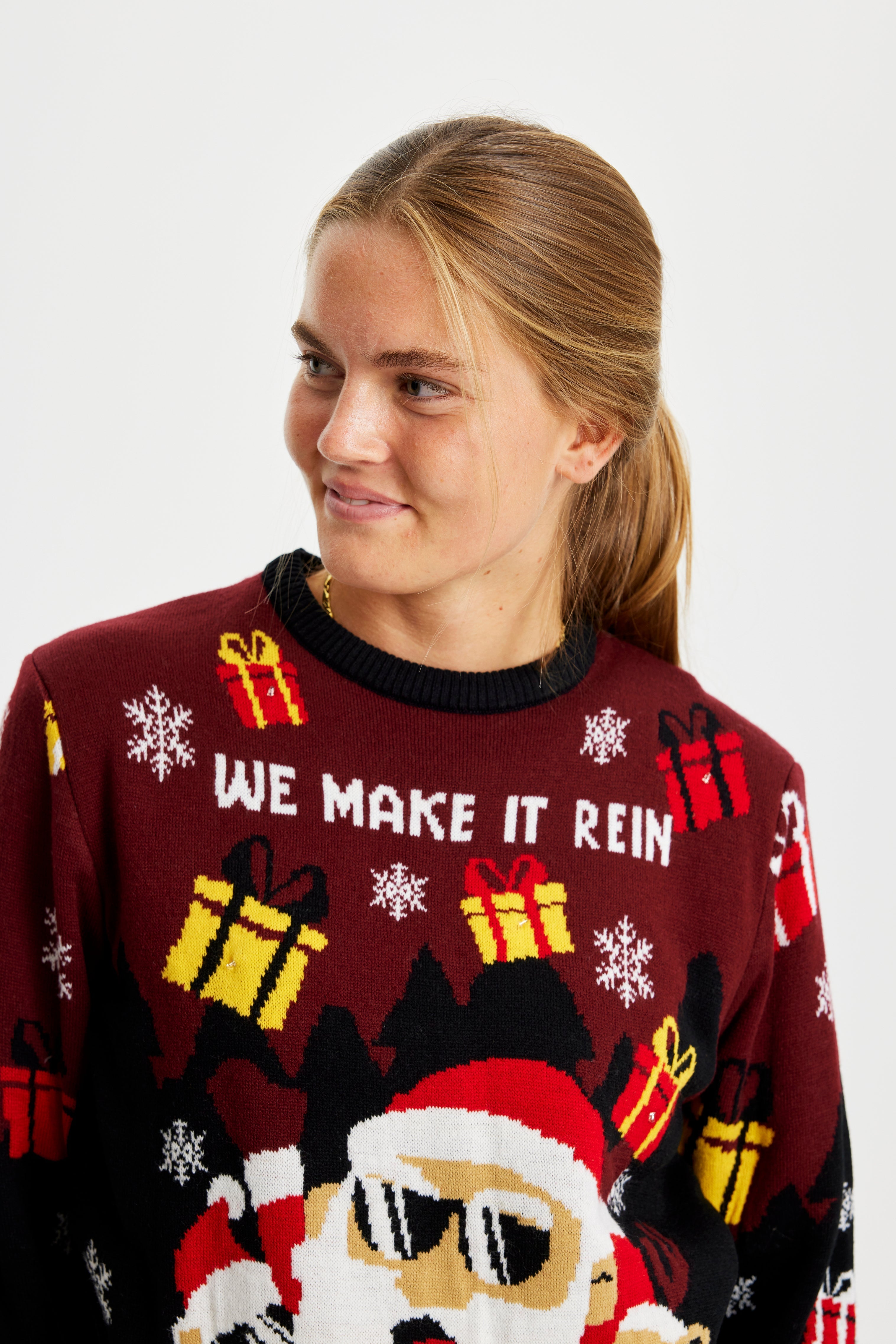 En kvinna som tittar åt sidan i en röd och svart jultröja med en jultomte med solglasögon och tända lampor.