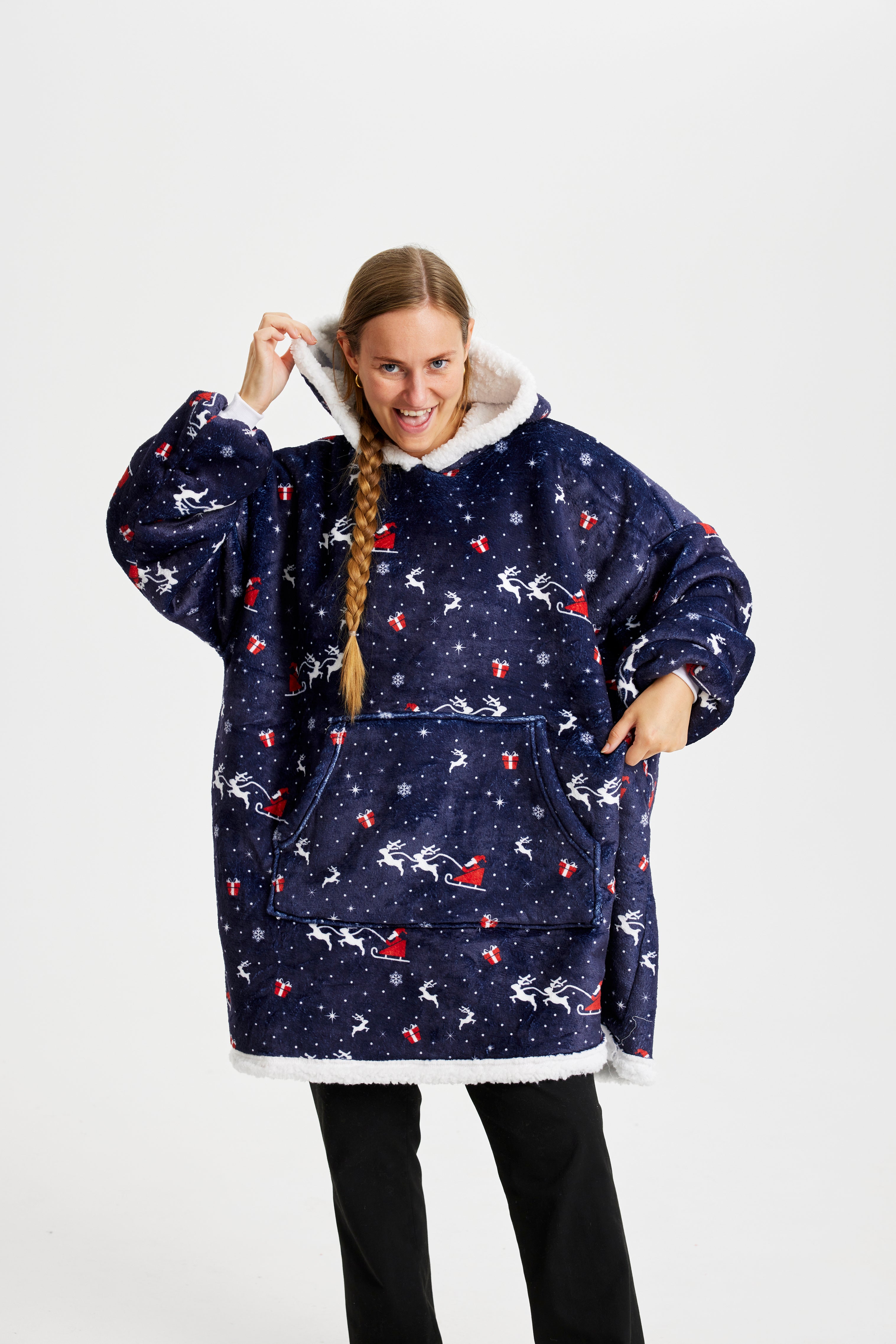 En poserande kvinna i mörkblå julhoodie med jultomten och hans släde.