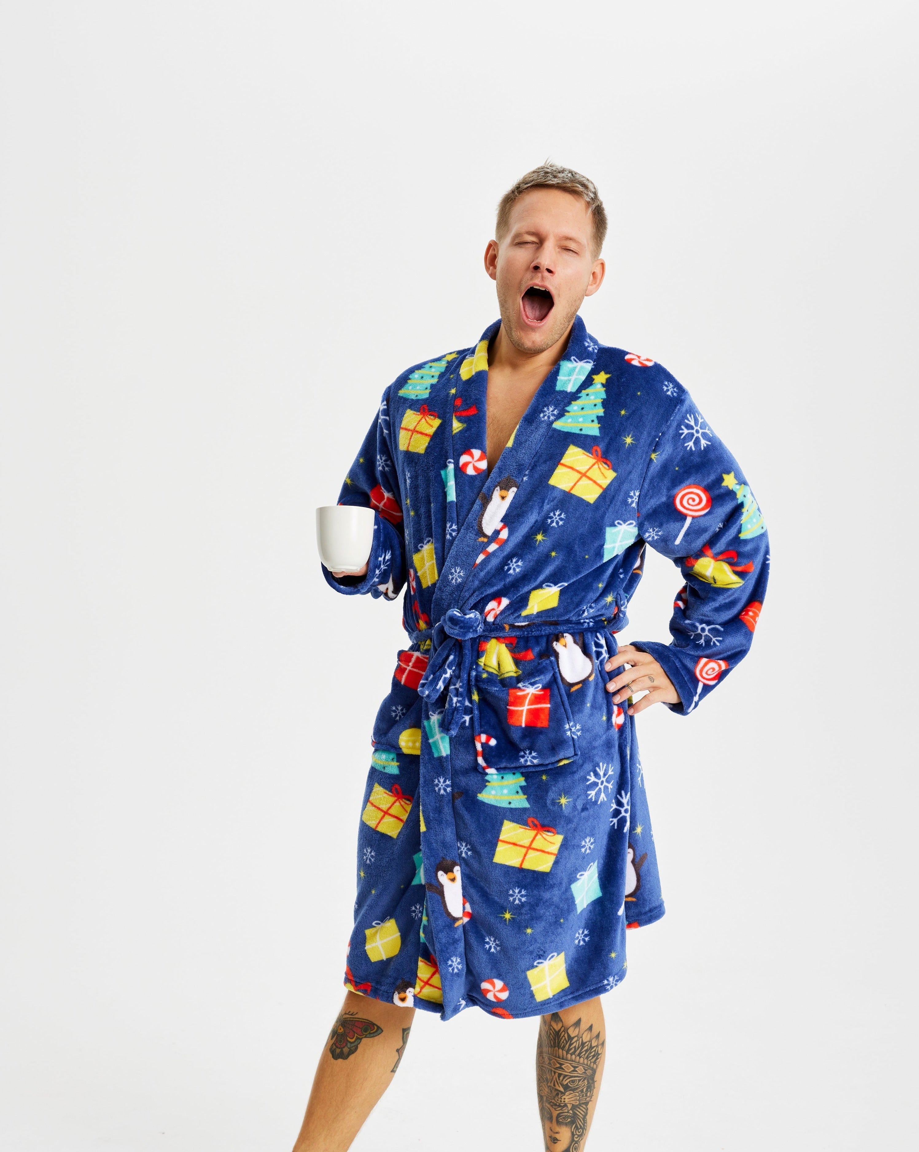 En gäspande man klädd i en blå morgonrock med julmotiv och presenter på.