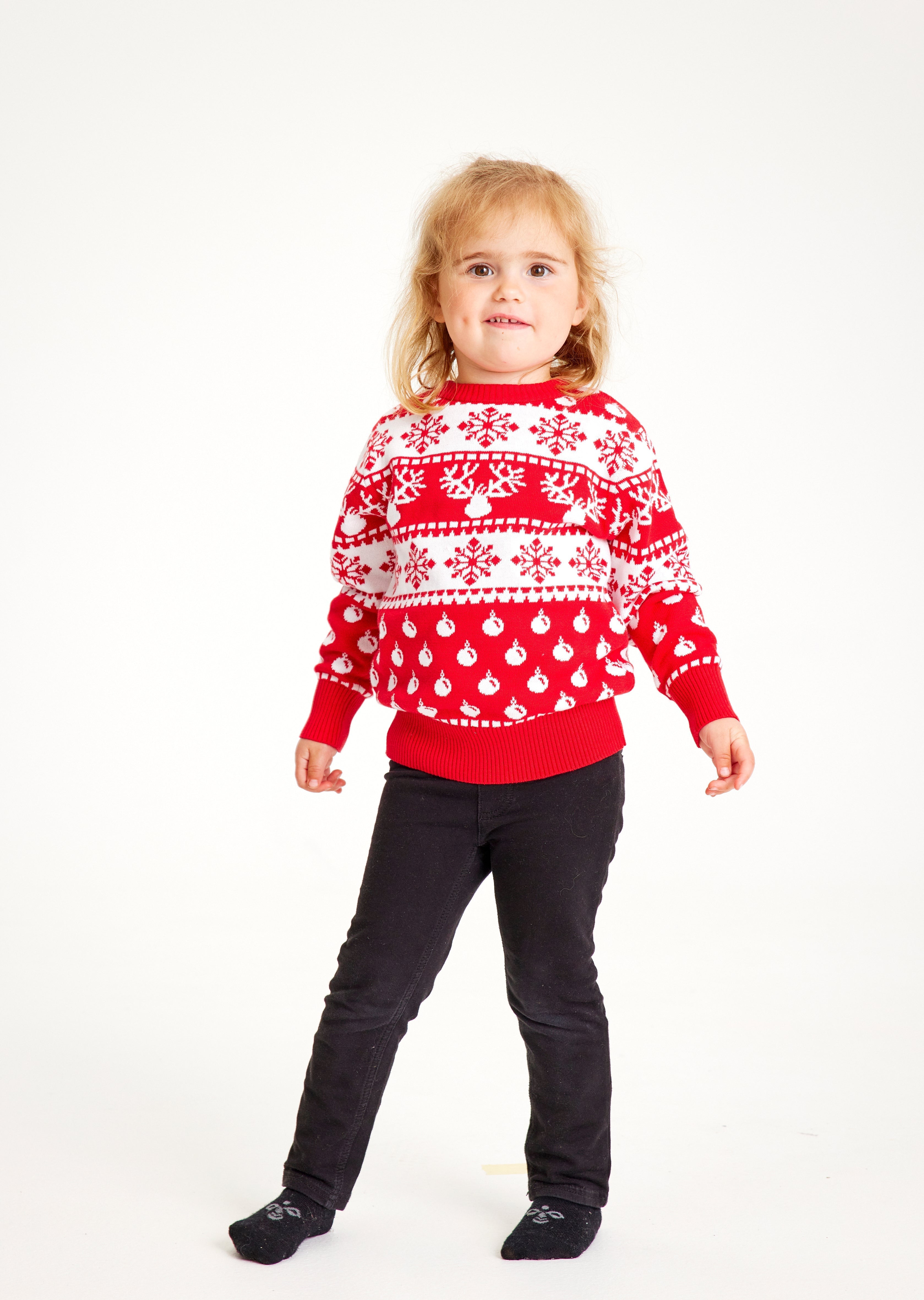 Poserande barn i röd jultröja med renar, snöflingor och julmönster.
