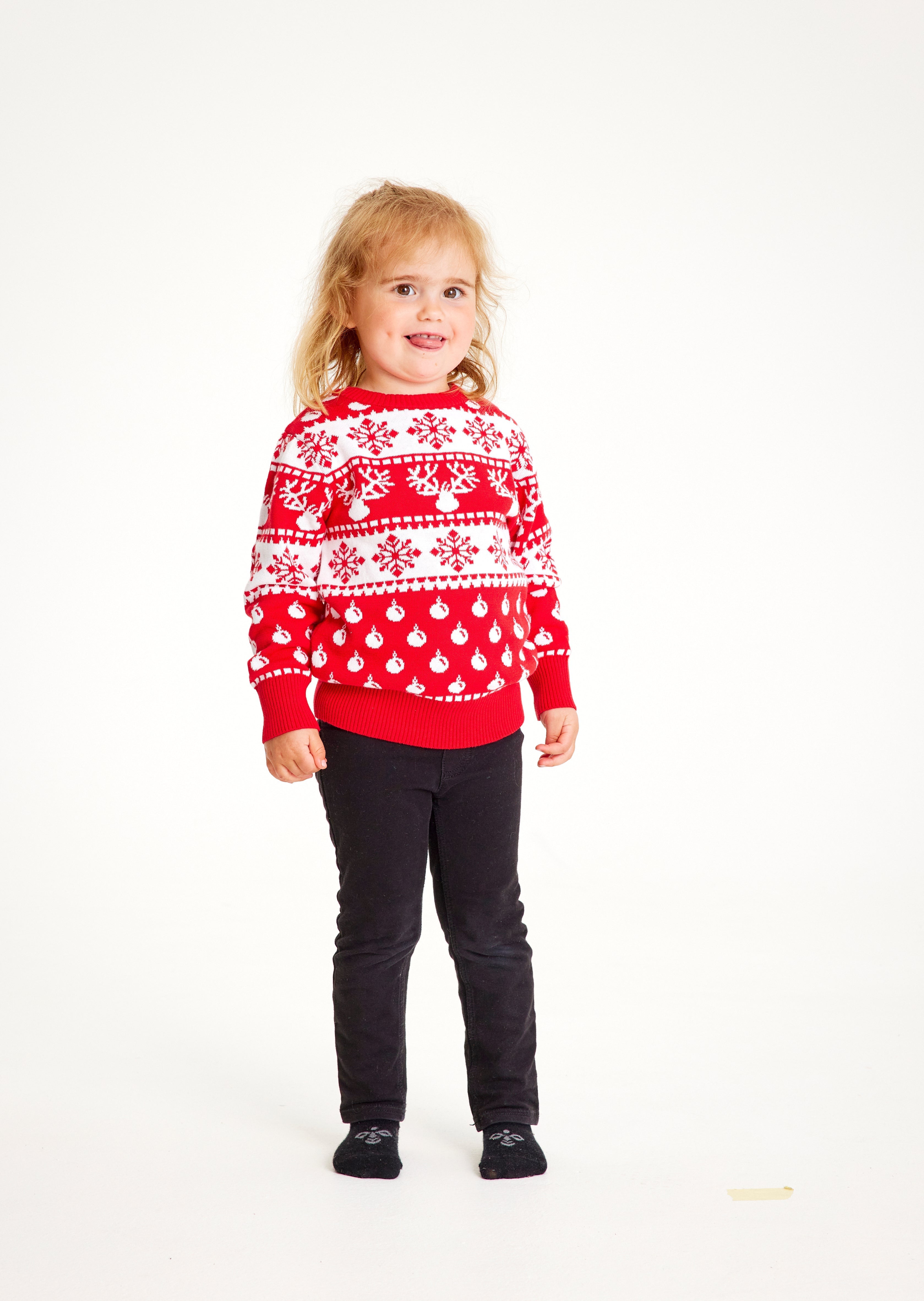 Ett barn i en röd jultröja med renar, snöflingor och ett juligt mönster.