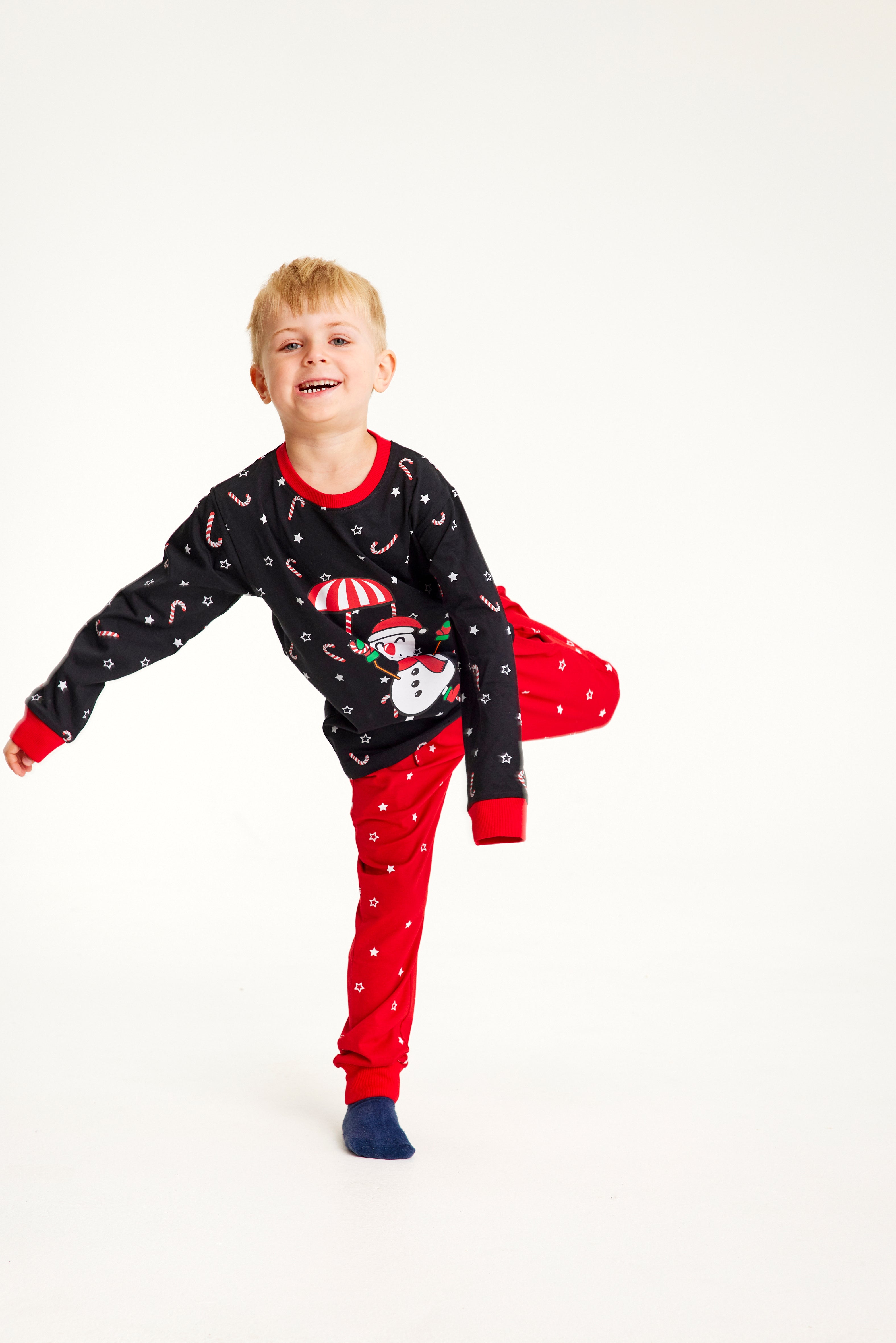 Ett barn på ett ben i röd och svart julpyjamas med en snögubbe på.