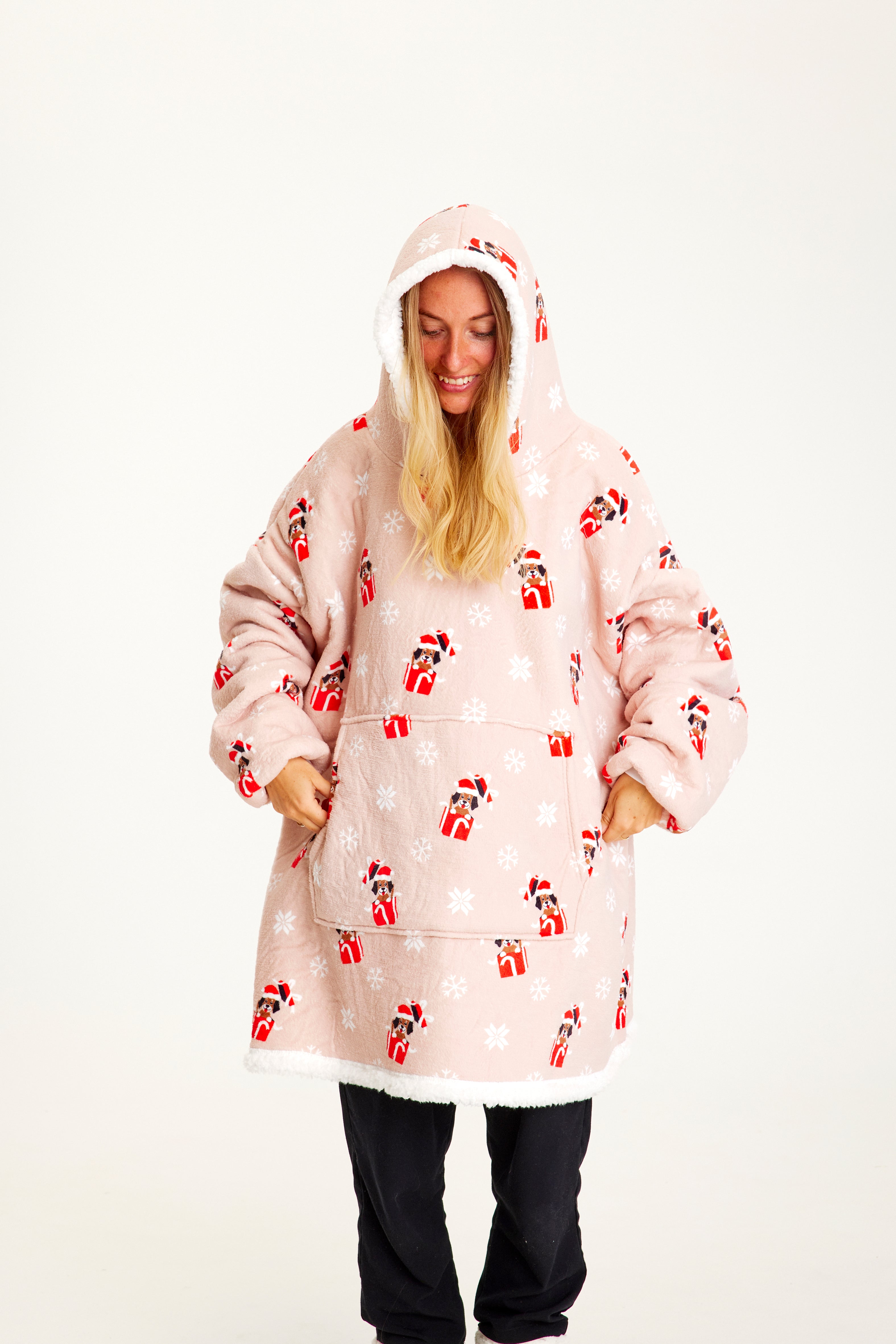 En leende kvinna med händerna i fickorna som bär en rosa huvtröja med julhundar på.